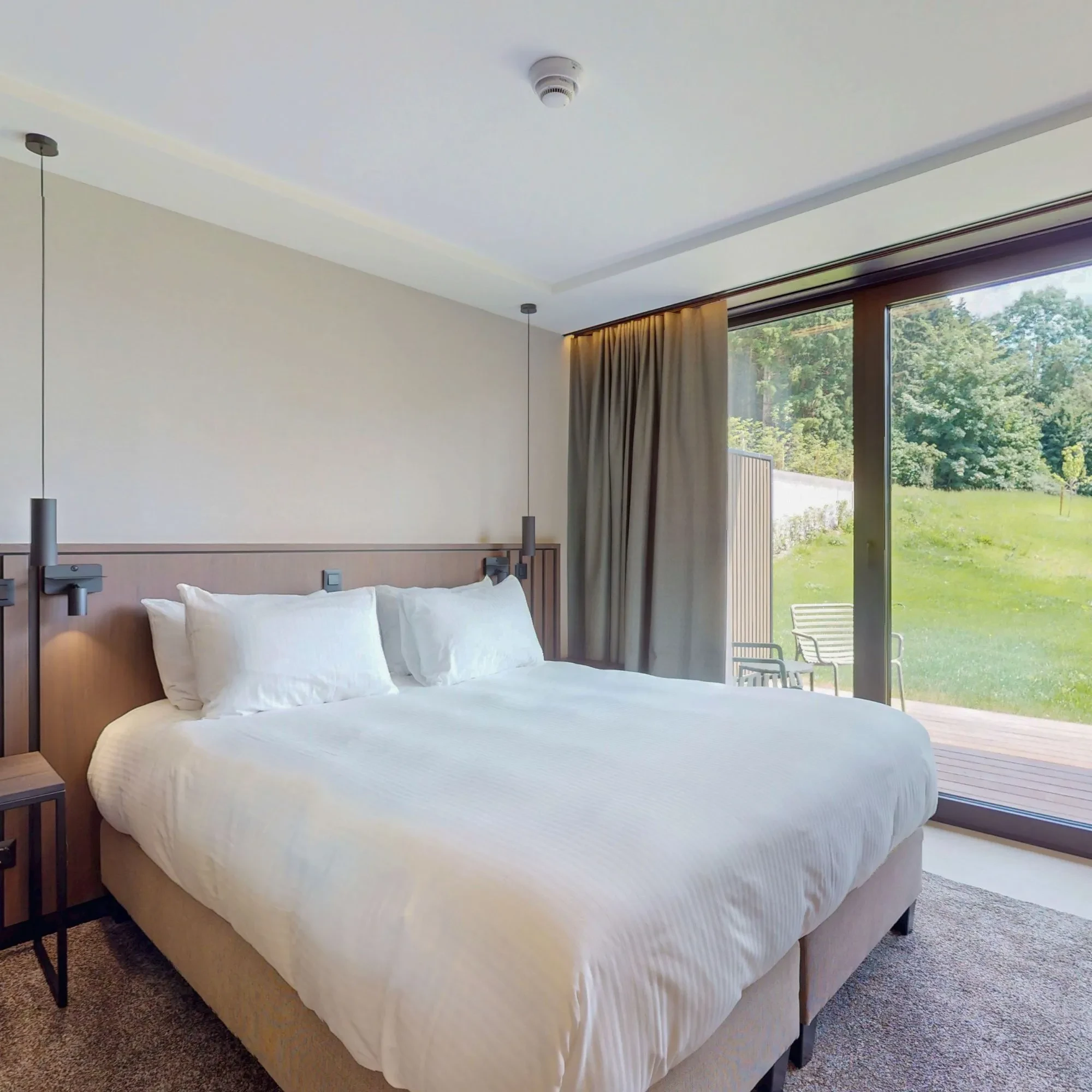 Chambre moderne avec lit, baie vitrée et jardin.